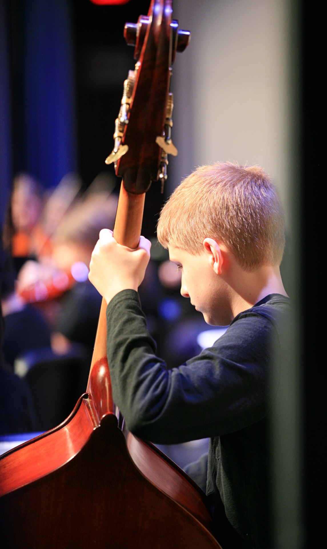 Young student carrying and playing an upright bass on stage